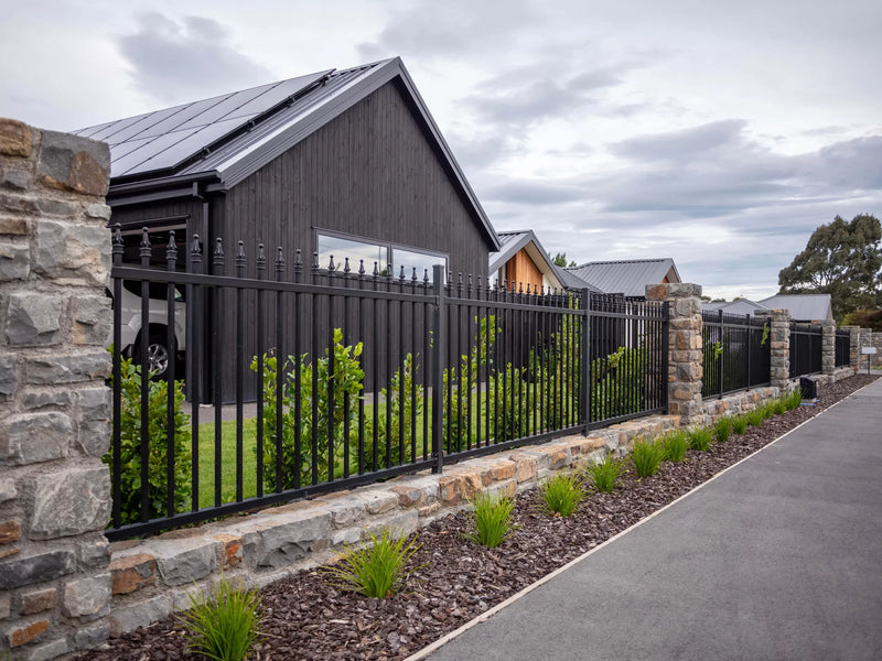 Modern house with a black metal fence and stone wall in a residential area.