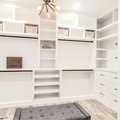 Modern walk-in closet with white shelves, drawers, and a gray bench.