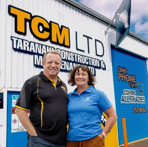 Two people standing in front of a building with 'TCM LTD' signage.