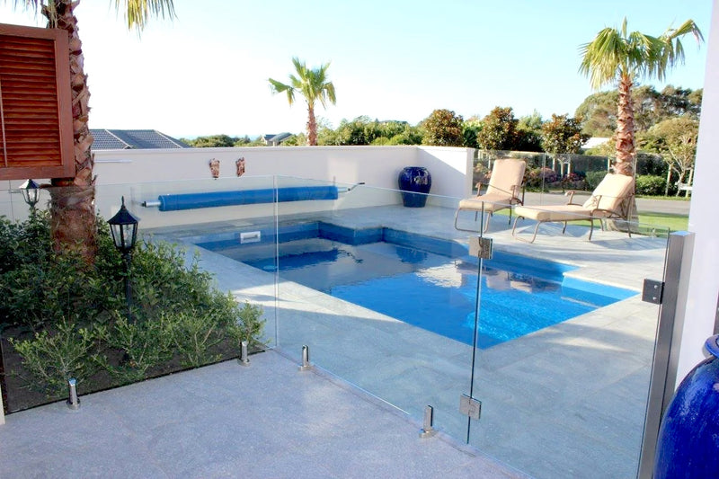 Modern pool with glass fence, lounge chairs, and palm trees in a sunny outdoor setting.