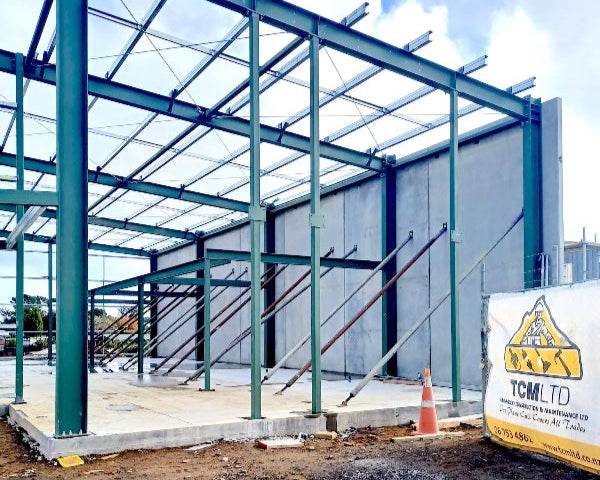 Under construction building with metal frame and visible branding on a dirt ground.