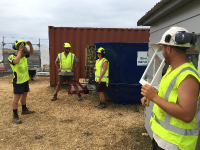 Workers in high-visibility vests and hard hats near a shipping container and blue tent.