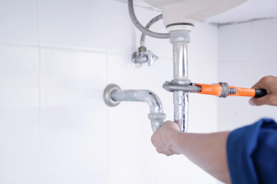 Person working on plumbing under a sink with a wrench.
