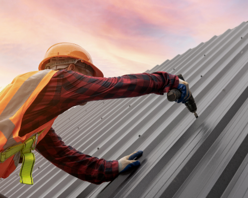 Person in safety gear drilling metal roofing panels with a colorful sky in the background