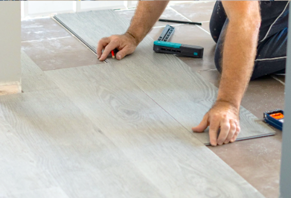Person installing wooden flooring with tools on a wooden floor.